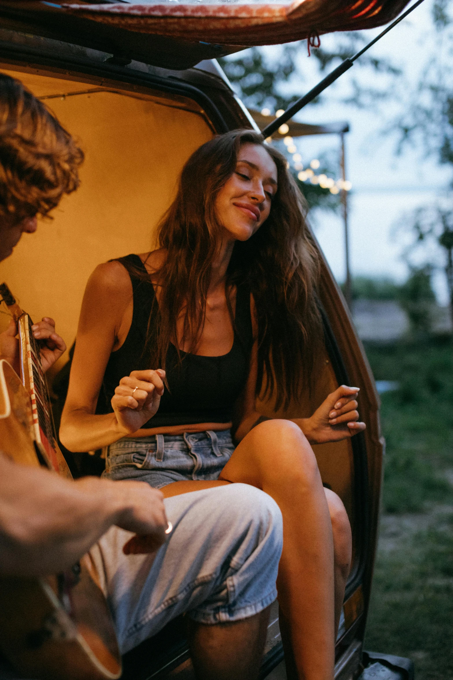 a man and a woman sitting in the back of a van, trending on pexels, renaissance, dancing around a fire, woman with braided brown hair, she is wearing a black tank top, guitar