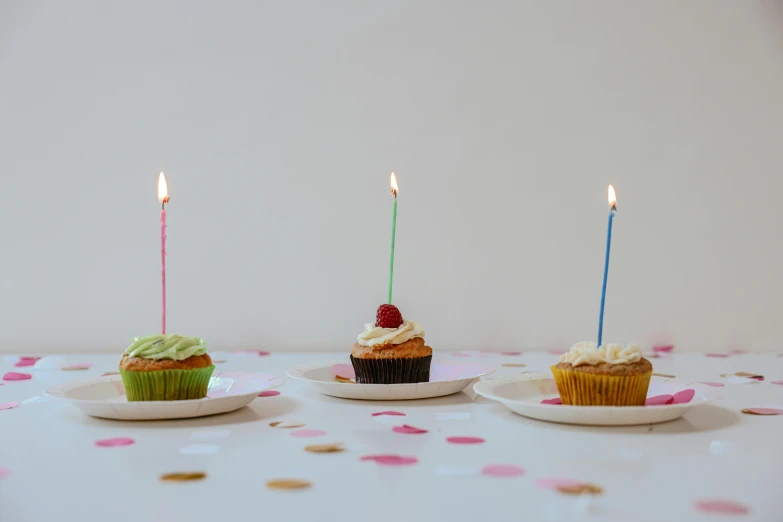 three cupcakes with lit candles sitting on plates, unsplash, hyperrealism, background image, multicoloured, minimalist photo, birthday party