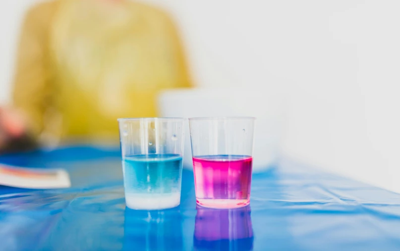 a couple of glasses sitting on top of a blue table, beakers of colored liquid, blue and pink shift, on a white table, split dye