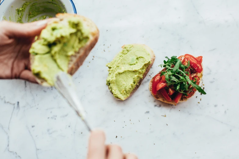 a person eating a piece of bread with avocado, by Carey Morris, trending on pexels, olive green and venetian red, basil, dwell, recipe