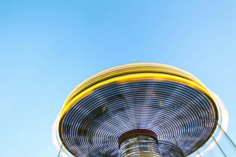 a close up of a ferris wheel with a blue sky in the background, by Matthias Stom, unsplash contest winner, magic realism, motion blur, yellow, flying saucer, shot on hasselblad