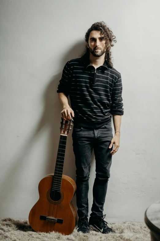 a man standing next to a guitar in a room, by Adam Dario Keel, on a gray background, mid long hair, nicholas kalmakoff, standing