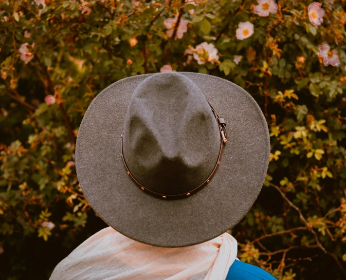 a person wearing a hat standing in front of a bush, pexels contest winner, profile image, western clothing, grey, seen from the back