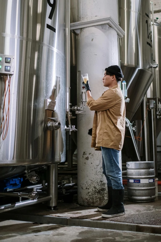 a man standing in front of a bunch of metal tanks, pexels contest winner, beer in hand, working, non-binary, brown