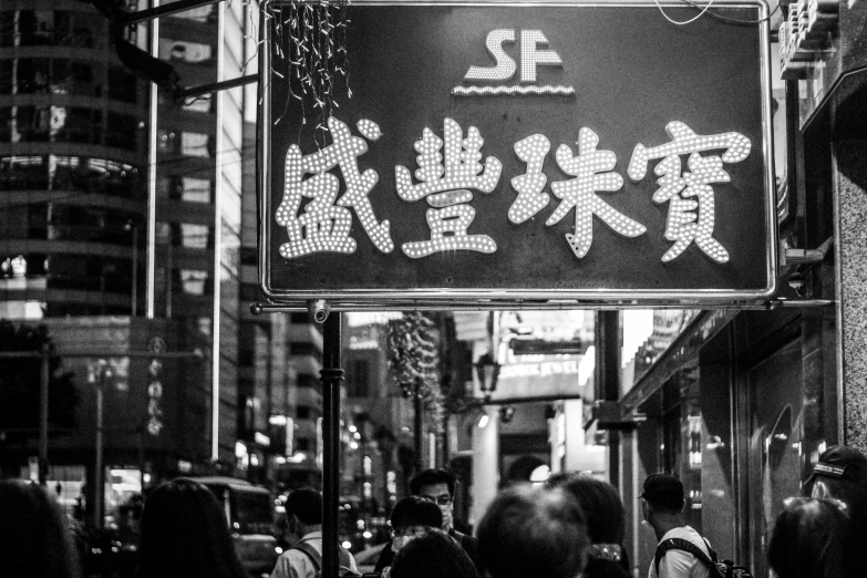 a group of people walking down a street next to tall buildings, a black and white photo, pexels, graffiti, golden chinese text, food stall, nighttime!, sign