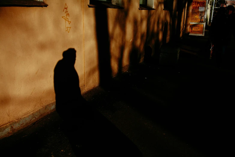 a shadow of a person standing in front of a building, by Attila Meszlenyi, pexels contest winner, realism, street of moscow, taken with kodak portra, in a suburb, hood and shadows covering face