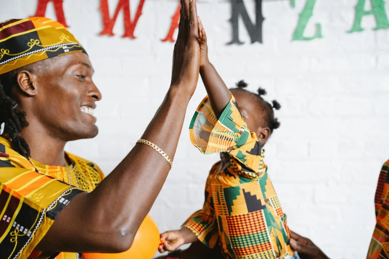 a woman holding a child up in the air, pexels contest winner, black arts movement, wearing an african dress, blessing hands, zulu, wearing red and yellow clothes