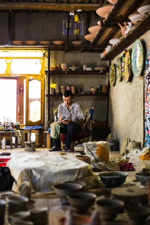 a man sitting in a room filled with pottery, process art, kurdistan, carefully crafted, in a workshop, vibrant scene