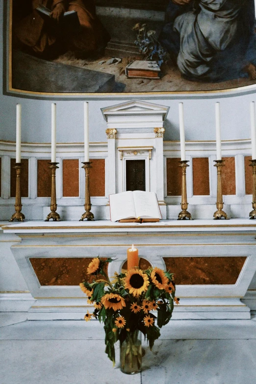 a vase of sunflowers in front of a painting, an album cover, by Cagnaccio di San Pietro, stone pews, candle lighting, white marble interior photograph, seasonal