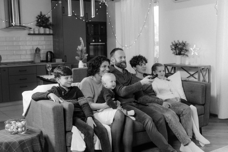 a black and white photo of a family sitting on a couch, pexels, festive atmosphere, tv footage, group of people, full body portrait of a group