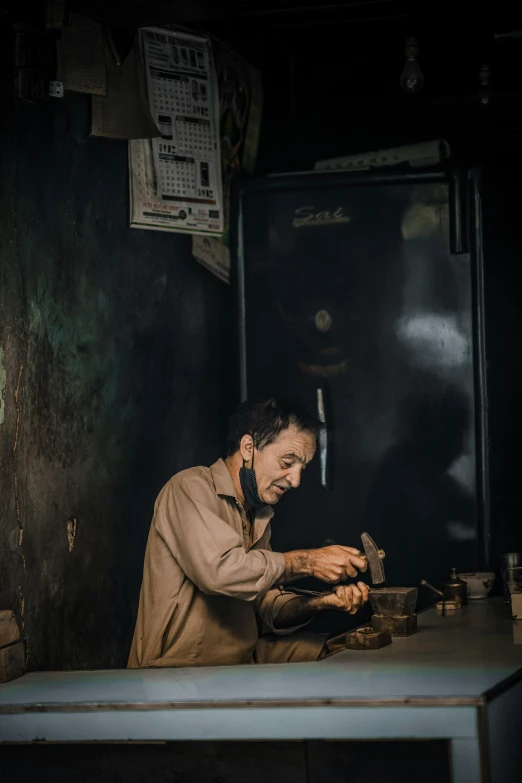 a man sitting at a table working on something, inspired by Steve McCurry, pexels contest winner, old charismatic mechanic, iraq nadar, phone photo, low-light