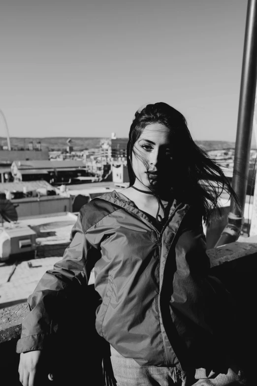 a black and white photo of a woman on a balcony, a black and white photo, unsplash, black haired girl wearing hoodie, rooftop party, ((messy)), she wears a jacket