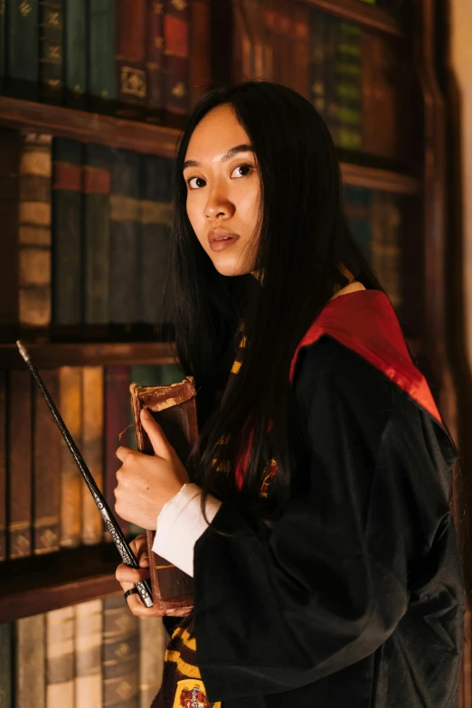 a woman standing in front of a bookshelf holding a wand, a portrait, pexels contest winner, asian girl with long hair, wearing hogwarts!!! robes!!!, promo image, academic clothing