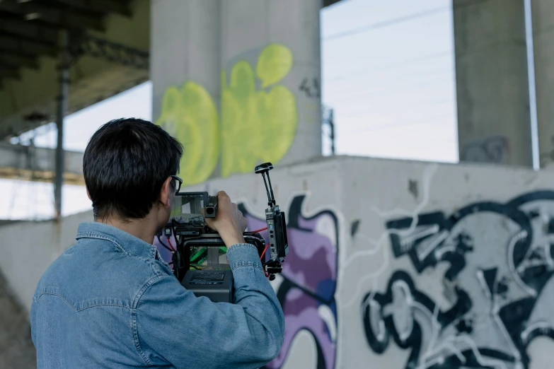 a man taking a picture of a graffiti covered wall, unsplash, graffiti, graded with davinci resolve, camcorder, cinematic outfit photo, crane shot