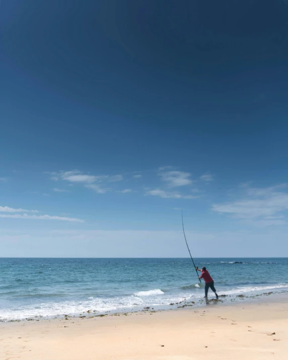 a man standing on top of a sandy beach next to the ocean, fishing pole, photo of the middle of the ocean, lachlan bailey, thumbnail