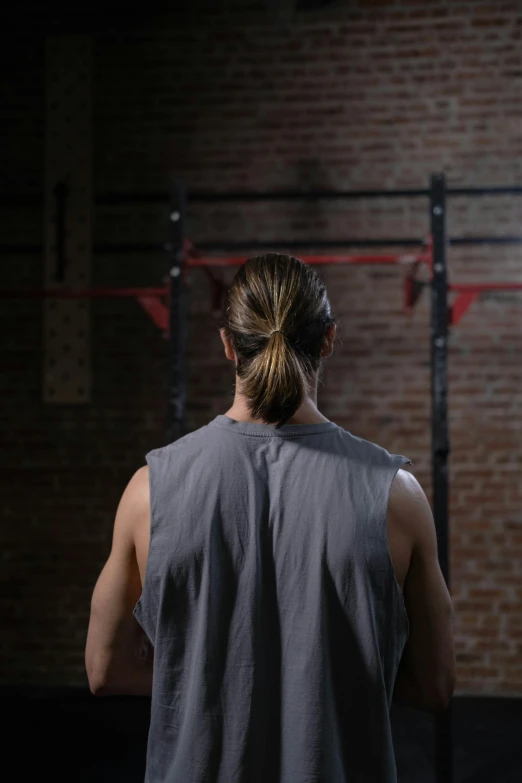 a man standing in front of a barbell in a gym, long braided hair pulled back, dark backround, back to camera, dustin lefevre
