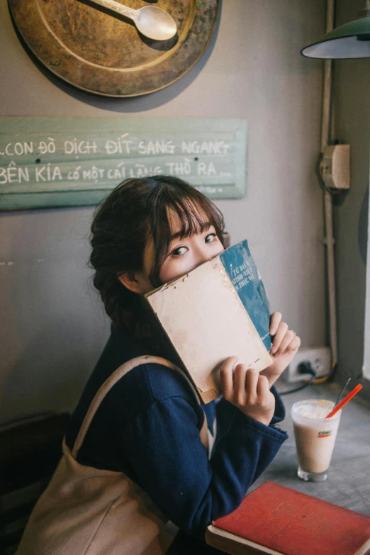 a woman sitting at a table reading a book, a picture, by Tan Ting-pho, unsplash contest winner, happening, wan adorable korean face, covered face, navy, ulzzang
