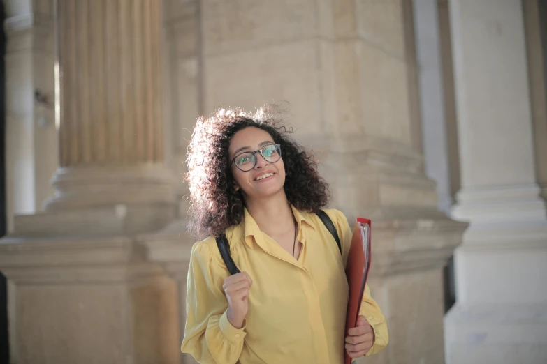 a woman in a yellow shirt holding a red book, pexels contest winner, young middle eastern woman, with a backpack, avatar image, architect