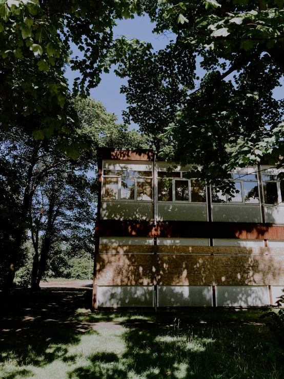 a tall building sitting on top of a lush green field, an album cover, by Emma Andijewska, unsplash, modernism, modern house in the wood, berlin park, 😭 🤮 💕 🎀, dappled afternoon sunlight