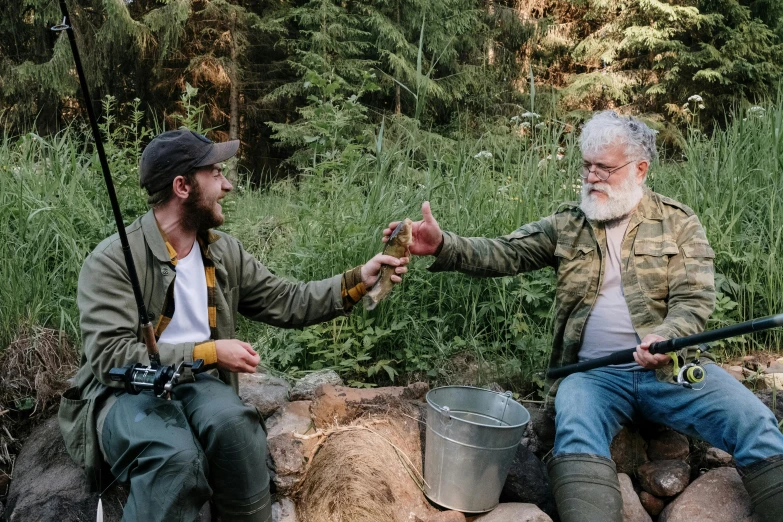 a couple of men sitting next to each other, by Jaakko Mattila, pexels contest winner, forest picnic, overalls and a white beard, two hands reaching for a fish, rhett and link