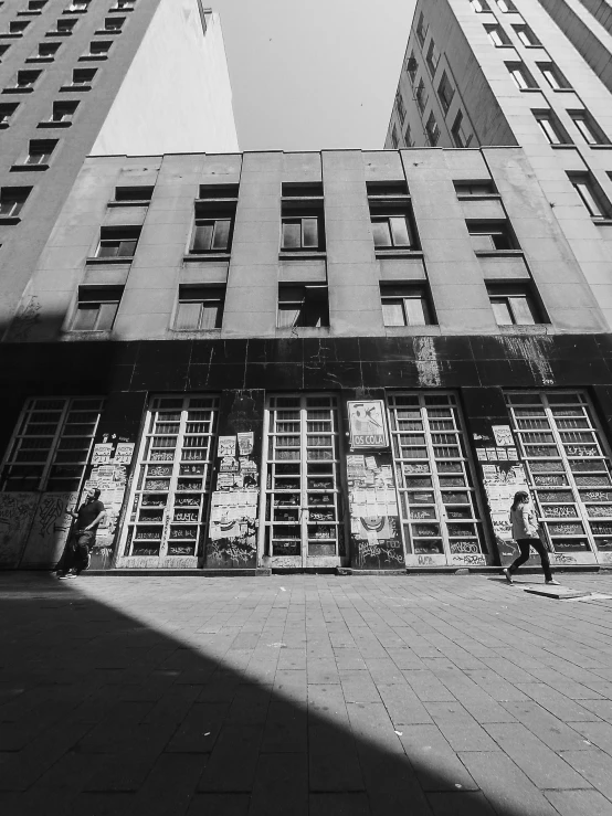 a black and white photo of two tall buildings, a black and white photo, by andrei riabovitchev, unsplash, brutalism, old shops, in empty!!!! legnica, cinematic. by leng jun, people walking around