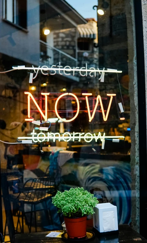 a woman sitting at a table in front of a window, temporary art, neon sign, tomorrow, now, shop front