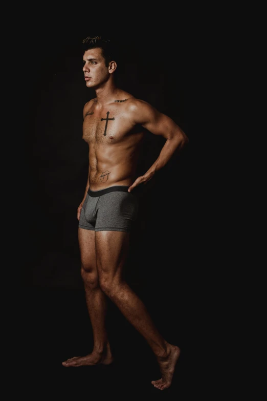 a man standing with his hands on his hips, a photo, inspired by Randy Vargas, gray shorts and black socks, dark backround, profile image, underwear ad