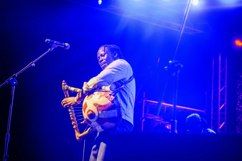 a man standing on top of a stage holding a guitar, emmanuel shiru, is playing a lute, profile image, bandoliers