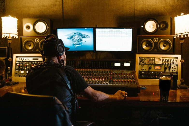 a man sitting at a desk in front of a computer, an album cover, by Matt Cavotta, pexels, private press, inside a grand studio, audio equipments, sitting at a control center, production i g