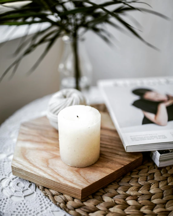 a candle sitting on top of a table next to a book, on a wooden tray, white marble interior photograph, looking towards camera, detailed product image