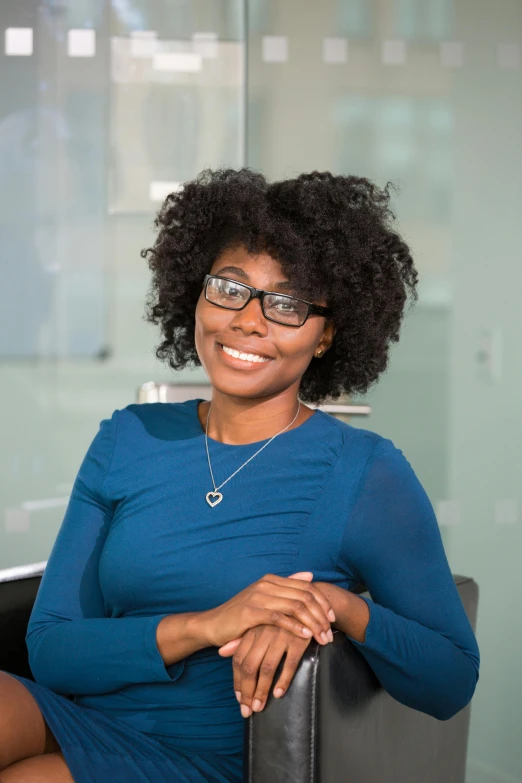 a woman in a blue dress sitting in a chair, afro tech, with glasses on, professional headshot, square