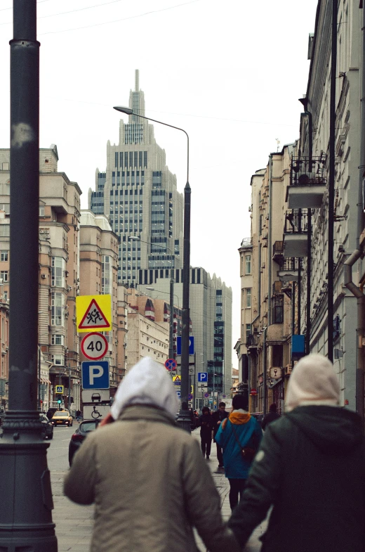 a group of people walking down a street next to tall buildings, by Adam Marczyński, russian style, high quality image, distant hooded figures, tourist photo