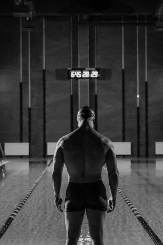 a man standing in the middle of a swimming pool, a black and white photo, rear side portrait of a muscular, strong lights, 1 0 0 m, countdown