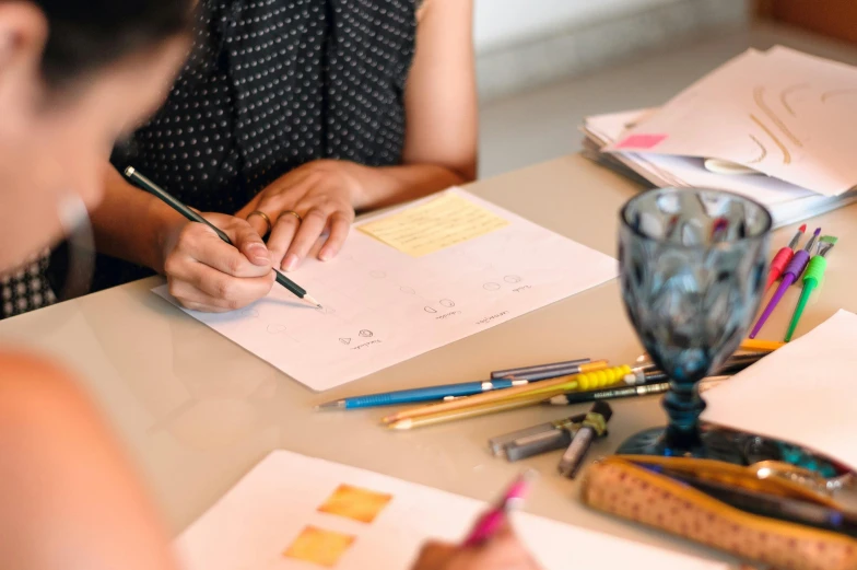 a woman sitting at a table writing on a piece of paper, a drawing, pexels contest winner, 9 9 designs, people at work, studious, no - text no - logo