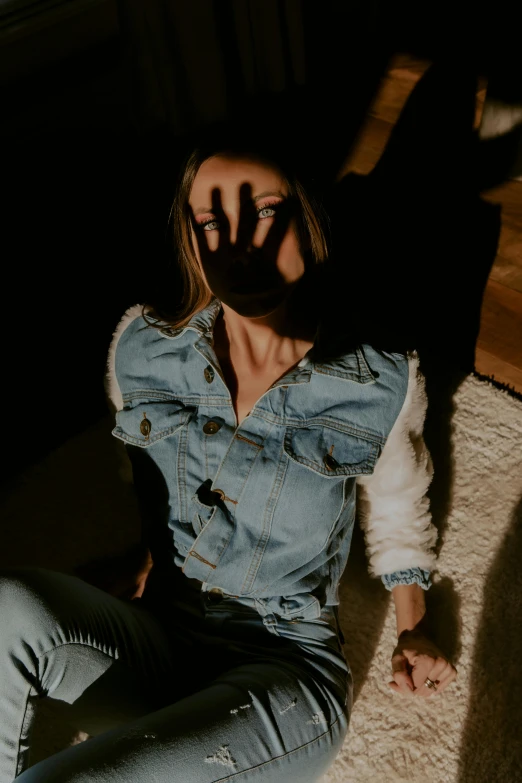 a woman sitting on the floor in a dark room, a picture, inspired by Elsa Bleda, trending on pexels, denim jacket, overhead sun, hands shielding face, long shadow