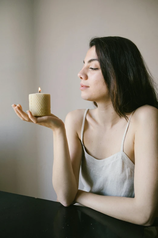 a woman sitting at a table holding a cup, inspired by Elsa Bleda, trending on unsplash, renaissance, on a candle holder, skincare, looking from side, studio photo