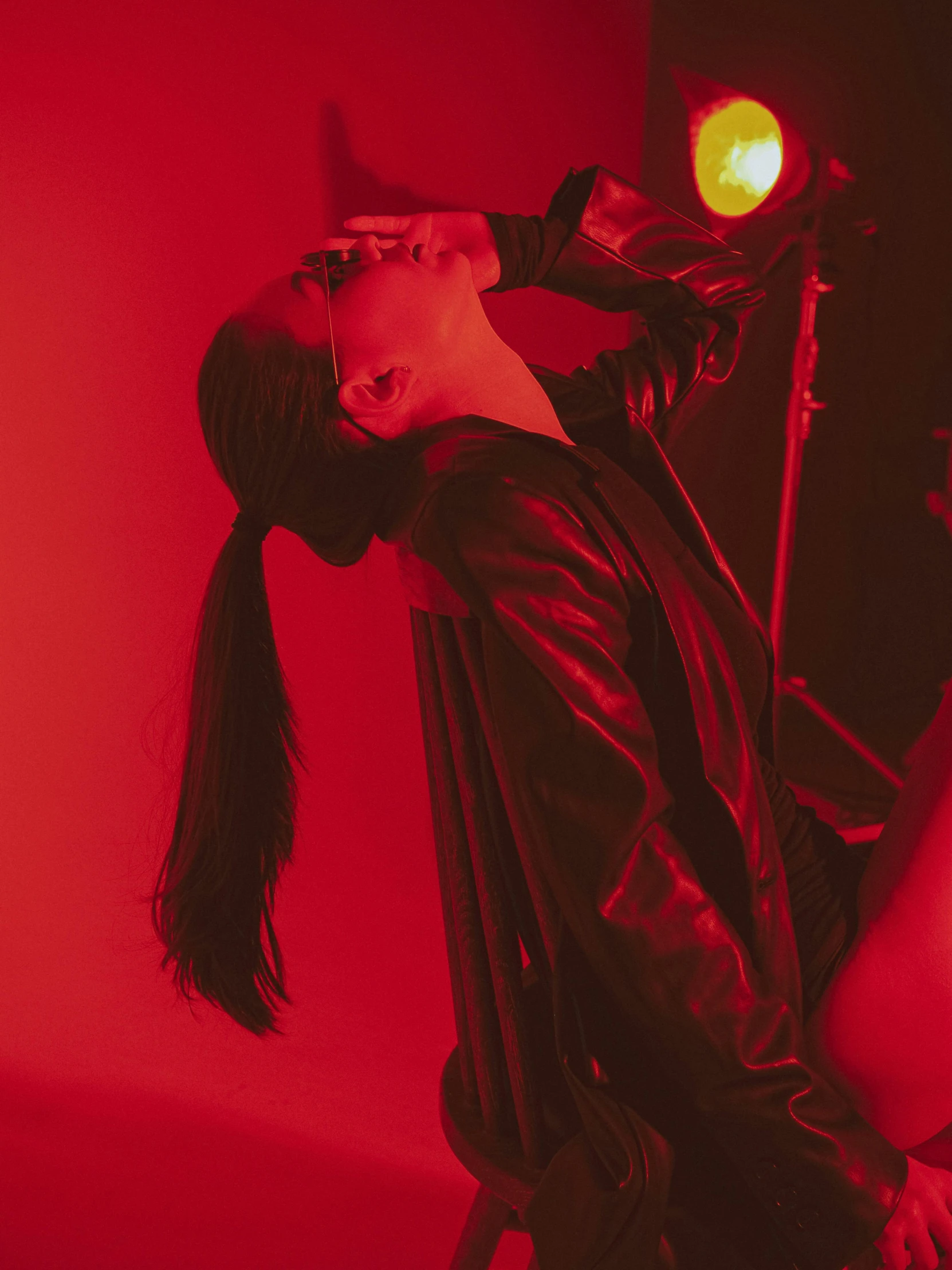 a woman sitting on a chair in front of a red light, long black ponytail, wonbin lee, profile image, leather clothing