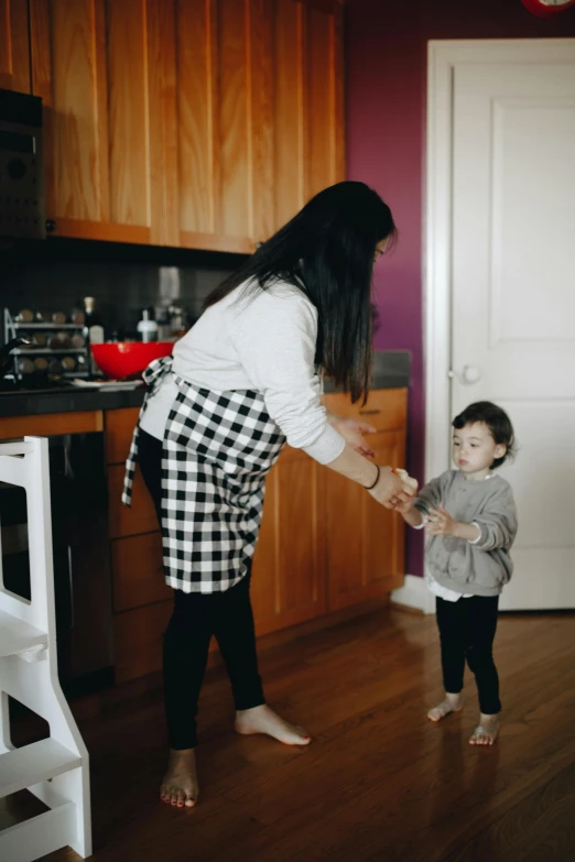 a woman holding a child's hand in a kitchen, happening, standing on two legs, manuka, brown, supportive