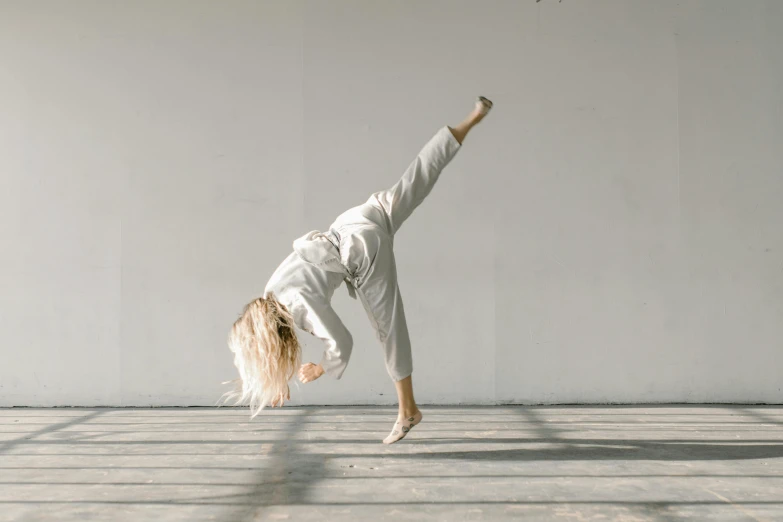 a woman doing a handstand in a white room, pexels contest winner, arabesque, wearing a track suit, a blond, posing for a fight intricate, whirling