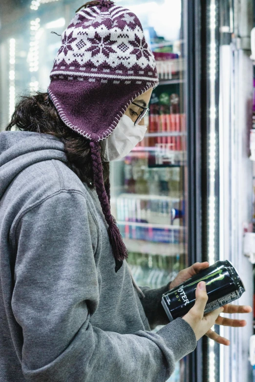 a woman in a face mask looking at a cell phone, pexels, graffiti, holding a can of beer, stood in a supermarket, he also wears a grey beanie, inuit