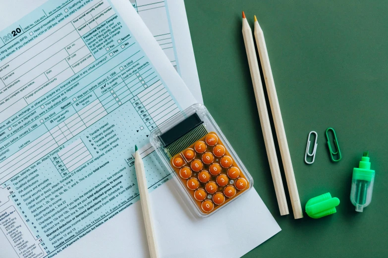 a calculator sitting on top of a table next to a pair of pencils, by Julia Pishtar, green and orange theme, sheet paper, thumbnail, medical supplies