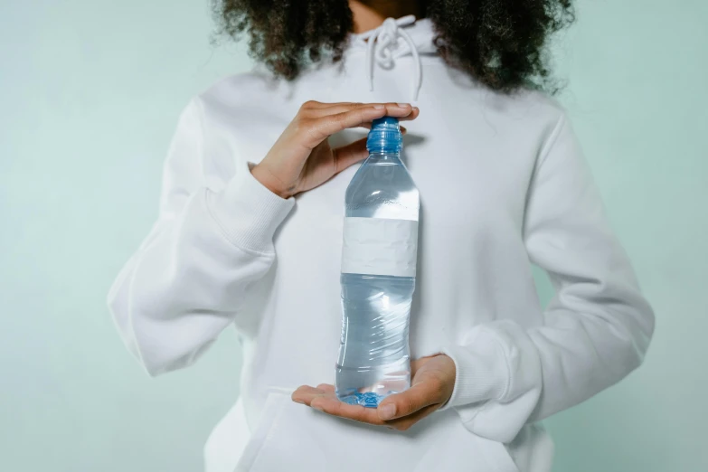 a woman holding a bottle of water in her hands, an album cover, pexels contest winner, plasticien, wearing a white sweater, thumbnail, hydration, plain background