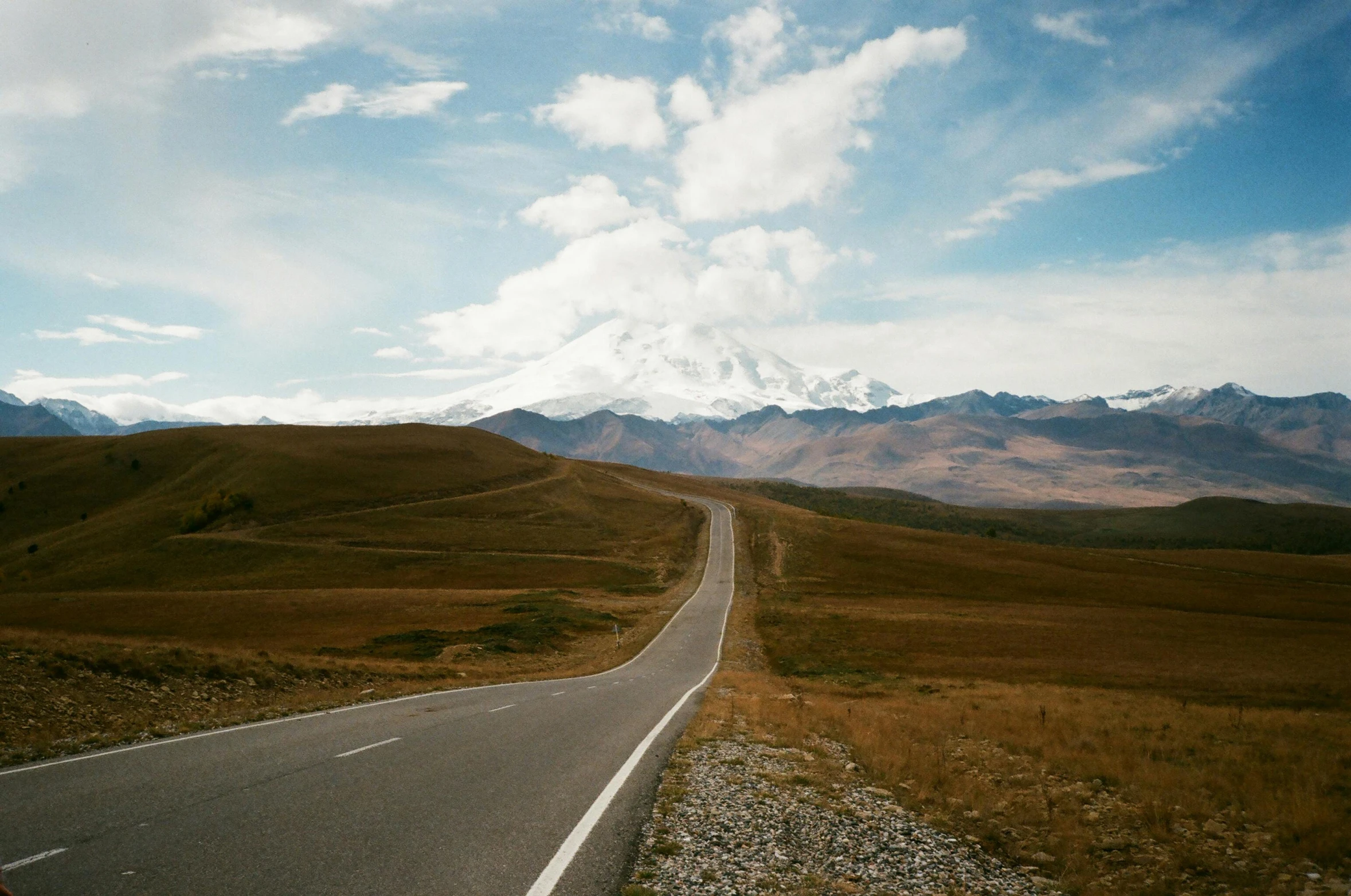 a road in the middle of a field with mountains in the background, unsplash contest winner, tengri, plain stretching into distance, profile image, wide high angle view