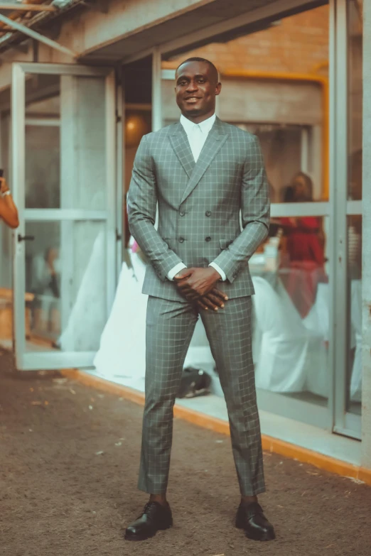 a man in a suit standing in front of a building, an album cover, inspired by David Bailly, pexels contest winner, happening, african man, wedding, grey skin, standing in a restaurant