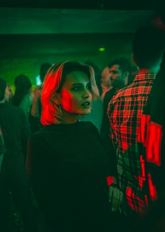 a woman standing in front of a crowd of people, an album cover, inspired by Elsa Bleda, trending on unsplash, happening, seductive smirk, chillin at the club together, red and green hour, intense look