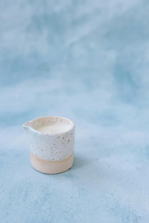 a small white cup sitting on top of a blue surface, by Ruth Simpson, textured base ; product photos, light pink mist, pestle, candle