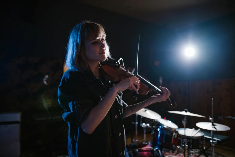 a woman playing a violin in a dark room, unsplash, concert, band, standing in a dimly lit room, lachlan bailey