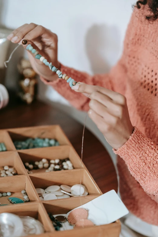 a woman in a pink sweater is holding a beaded necklace, trending on pexels, arts and crafts movement, stitching, turquoise, animation, cardboard