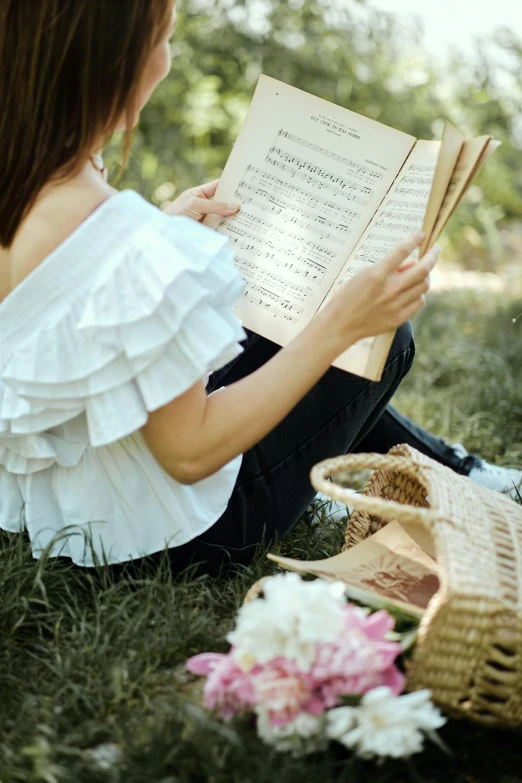 a woman sitting in the grass reading a book, an album cover, pexels contest winner, romanticism, sheet music, wearing a white blouse, picnic, plays music