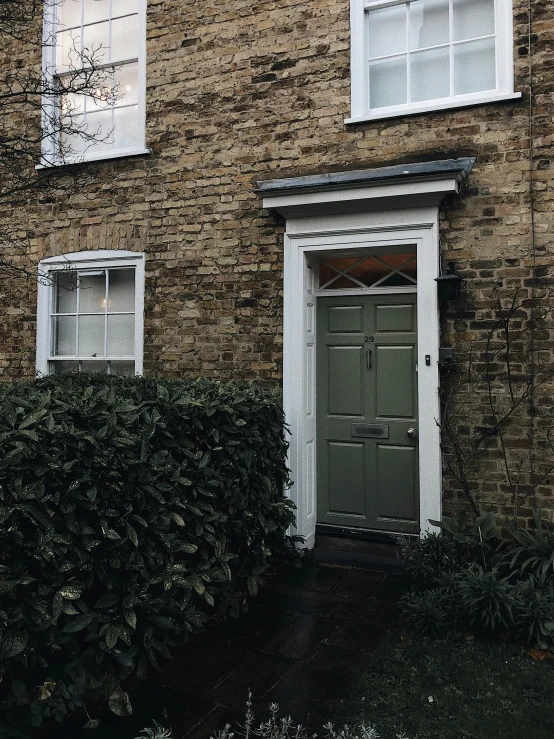 a brick building with a green door in front of it, inspired by Rachel Whiteread, unsplash, hedge, grey and gold color palette, low quality photo, my home